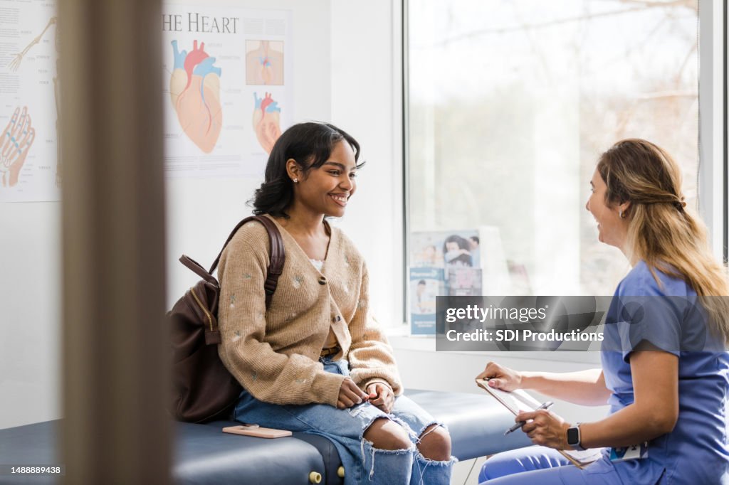 Young adult female patient smiles while listening to the nurse give an encouraging update regarding her medical exam