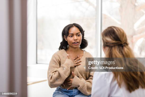 eine studentin bewegt sich in richtung ihrer brust, als sie das unbehagen beschreibt, das sie erlebt hat - speaking explaining young woman stock-fotos und bilder