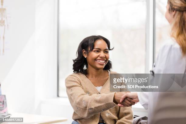 teen girl greets doctor with toothy smile and handshake - pregnant women greeting stockfoto's en -beelden