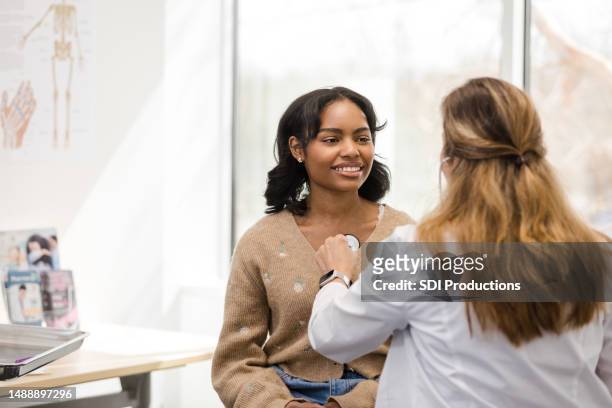 female university student smiles as unrecognizable female doctor uses stethoscope - ssc exam stock pictures, royalty-free photos & images