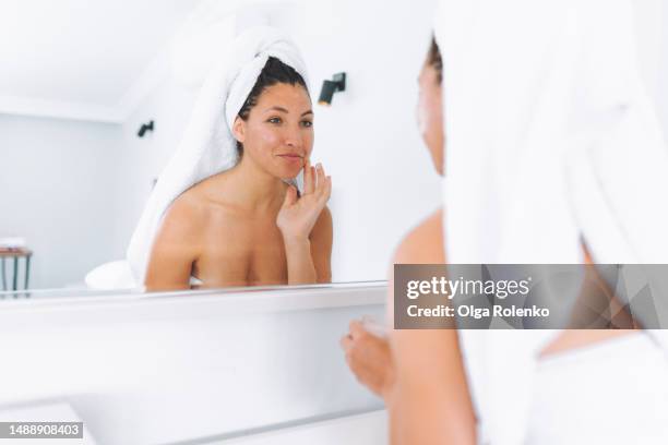 acne cream and face cleansing morning routine. woman taking care of her complexion, applying moisturizing cream and lotion for a youthful look in white bathroom - perfect complexion stock pictures, royalty-free photos & images