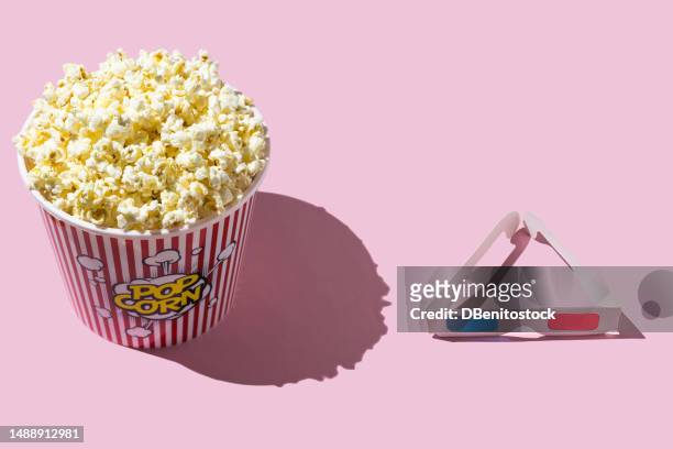 plastic container of popcorn next to retro 3d glasses with red and blue lenses, on a pink background. cinema, entertainment, film, show, fat, food, fast food and fatness concept. - european film awards imagens e fotografias de stock