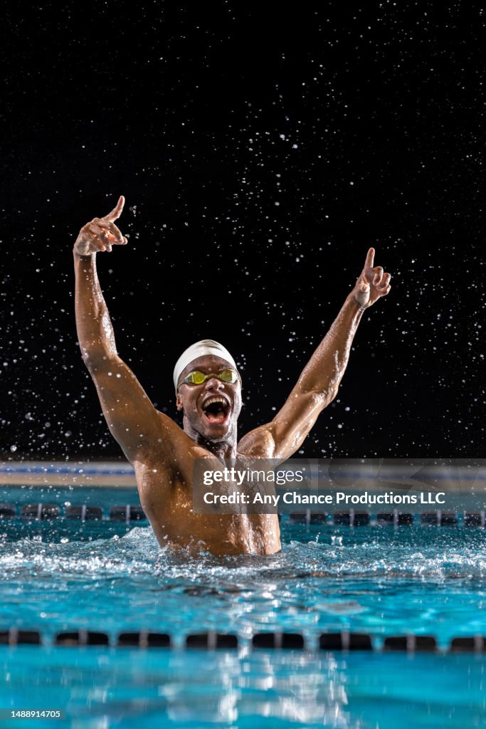 Male black swimmer raises his arms after winning a race.