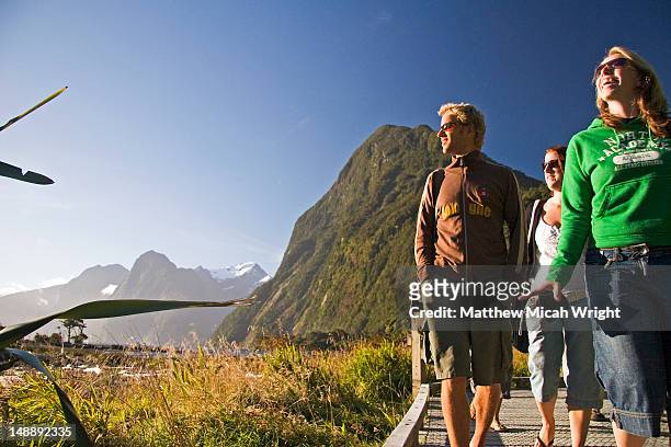 tourists walking through milford sound with mitre peak in background. - fjord milford sound stock-fotos und bilder