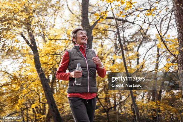 senior woman jogging in park - middle age active lifestyle stock pictures, royalty-free photos & images