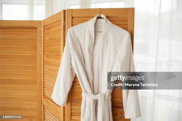 a white terry robe hangs on a hanger. home clothes. - accappatoio foto e immagini stock