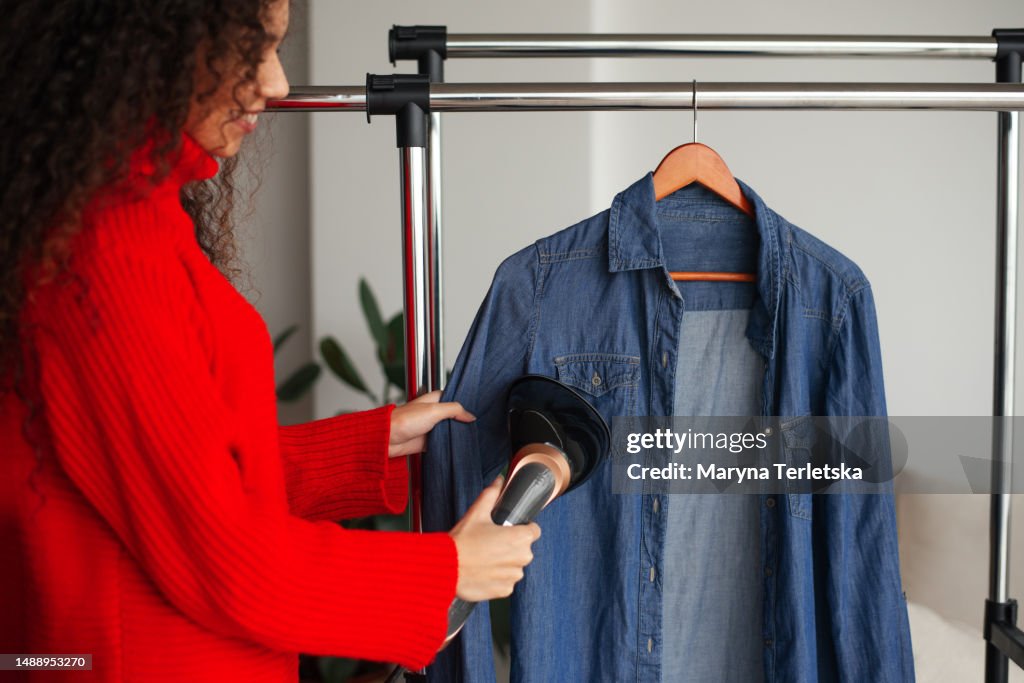 A black woman is steaming her shirt. Household chores. Ironing clothes. Caring for clothes.