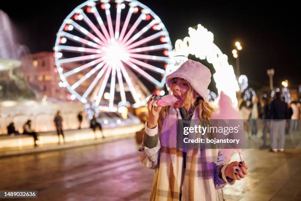 young woman eating cotton candy in amusement park - amusement park ride stockfoto's en -beelden