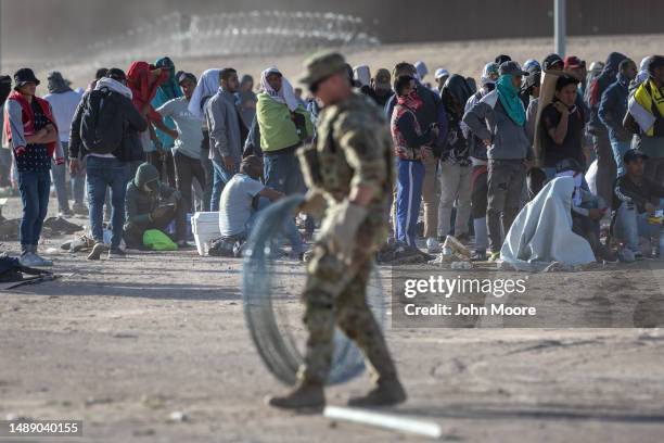 Immigrants watch as a Texas National Guard soldier prepares to uncoil razor wire around a makeshift immigrant camp located between the Rio Grande and...