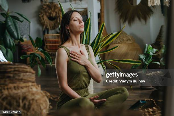 woman with closed eyes practising breathing exercises sitting lotus pose at home - woman breathe stock pictures, royalty-free photos & images