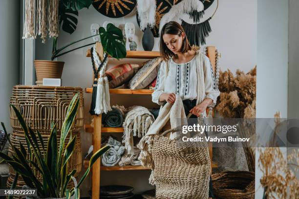 young woman putting fabrics in a wicker basket in her cozy home - laundry basket fotografías e imágenes de stock