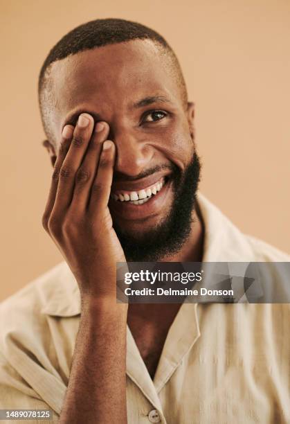 portrait head shot of a black man with his hand over one eye with a wide smile, stock photo - omlaag kijken stockfoto's en -beelden