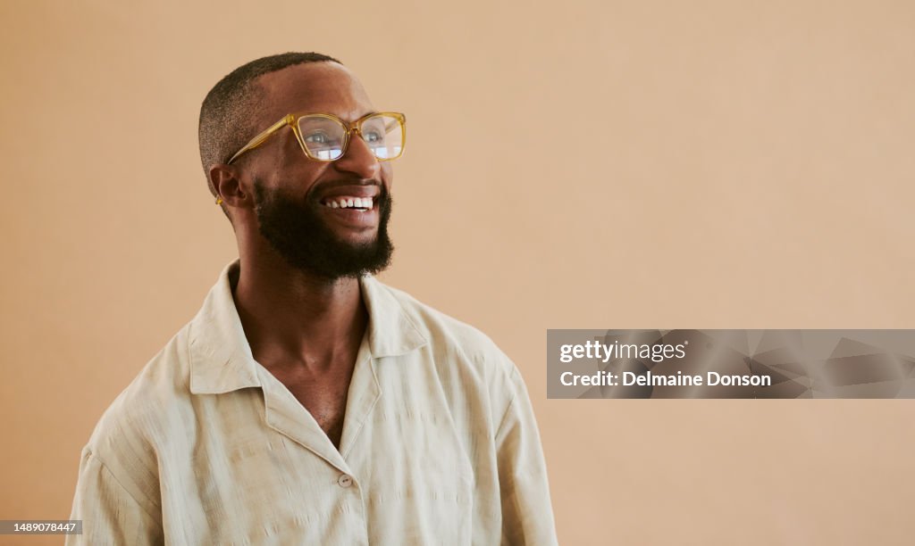Happy young black man standing whilst wearing eye glasses and a brown shirt whilst looking away from the camera with copy space, stock photo