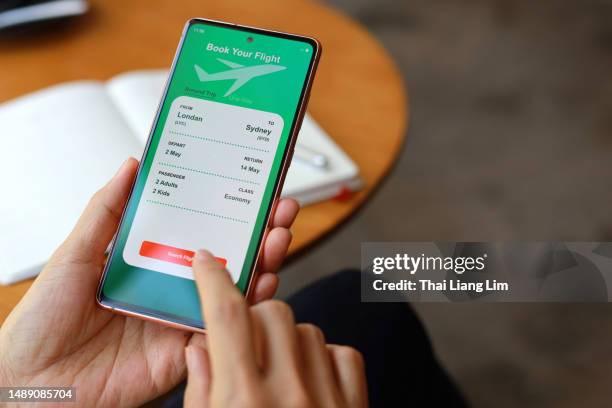 an over-the-shoulder view captures a woman using a smartphone application to book flight tickets and plan her holiday trip. - and booking com application stock pictures, royalty-free photos & images