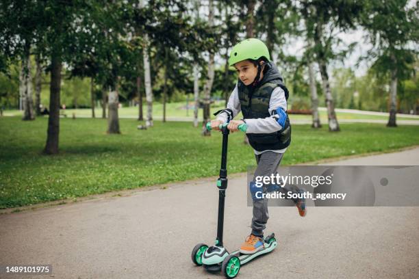 little boy riding a push scooter in the park - trotinete imagens e fotografias de stock