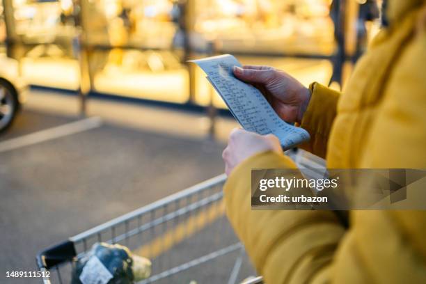 young woman looking at the receipt from the grocery store - grocery receipt stock pictures, royalty-free photos & images