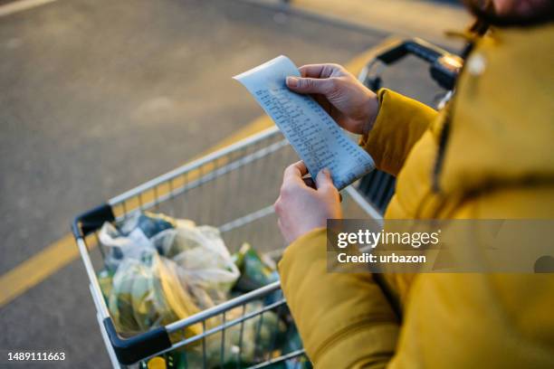 junge frau schaut auf die quittung aus dem lebensmittelgeschäft - kassenbon stock-fotos und bilder