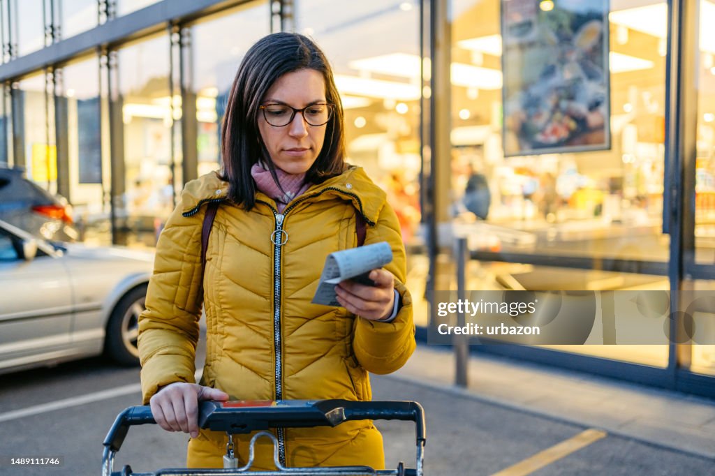 Young Woman Looking At The Receipt After Getting Out Of The Grocery Store