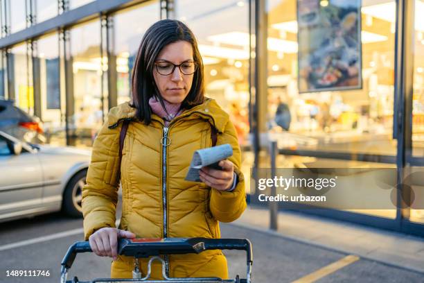 young woman looking at the receipt after getting out of the grocery store - expense receipts stock pictures, royalty-free photos & images