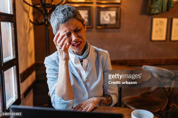 ältere geschäftsfrau hat zahnschmerzen, während sie in einem café am laptop arbeitet - toothache stock-fotos und bilder