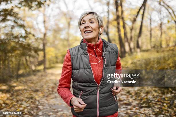 senior woman jogging in park - fall park stock pictures, royalty-free photos & images