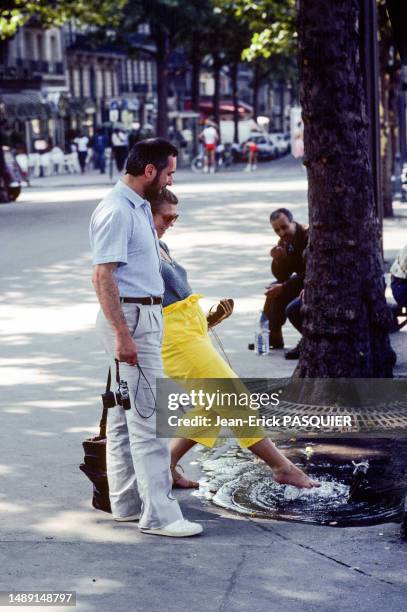 Une femme se rafraichit les pieds dans une flaque d'eau au pied d'un arbre en temps de canicule en septembre 1981 à Paris.