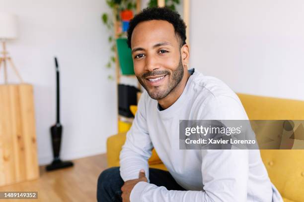 confident happy young adult man smile at camera sitting on sofa at home. - dominican ethnicity stock pictures, royalty-free photos & images