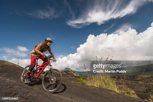 male downhill biker riding mountain bike down volcanic ridge - kintamani stock pictures, royalty-free photos & images