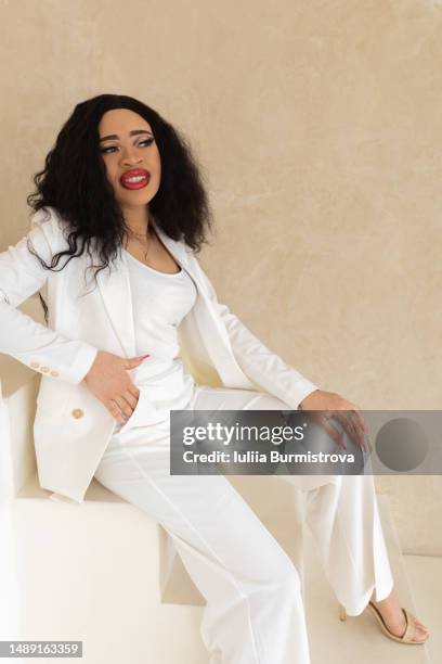 young female person of color with long black hair in white pant suit sitting on white stairs - artificial nails stock pictures, royalty-free photos & images