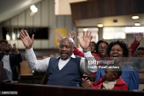 gemeinde mit geschlossenen augen und erhobenen armen betet in der kirche - congregation stock-fotos und bilder