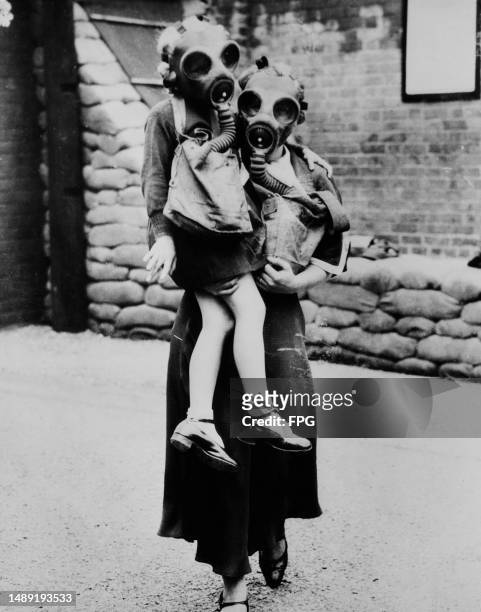 Mother carries her daughter while both wearing gas masks, Britain, circa 1915.
