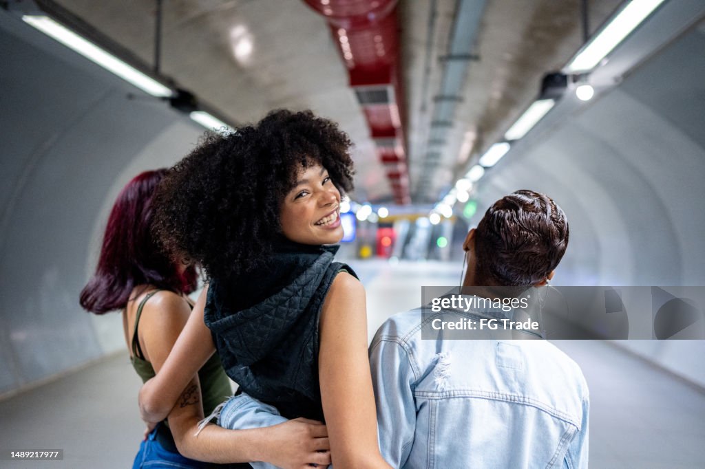 Retrato de una mujer joven caminando mientras abraza a sus amigos en la estación de metro