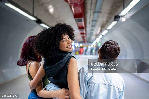 portrait of a young woman walking while embracing her friends at the subway station - black culture stock pictures, royalty-free photos & images