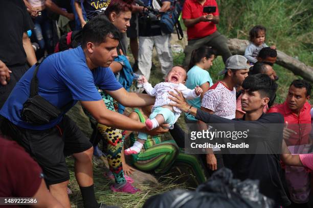 Baby is passed between people as migrants make their way into the Rio Grande as they cross to enter the United States on May 11, 2023 in Matamoros,...