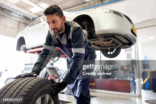 Glücklicher Mechaniker, der einen platten Reifen an einem Auto wechselt Glücklicher Mechaniker, der einen platten Reifen an einem Auto wechselt