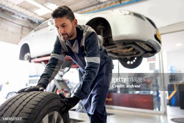 車のパンクしたタイヤを交換する幸せな整備士 - 自動車修理工場 ストックフォトと画像