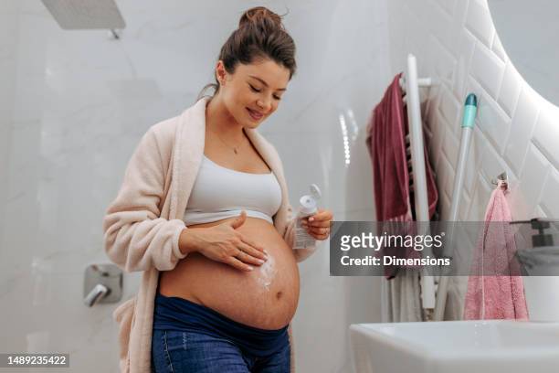 pregnant woman applying cream on belly. - stretch mark stock pictures, royalty-free photos & images