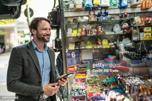 mature man paying with mobile phone in a newsstand - tidningsstånd bildbanksfoton och bilder