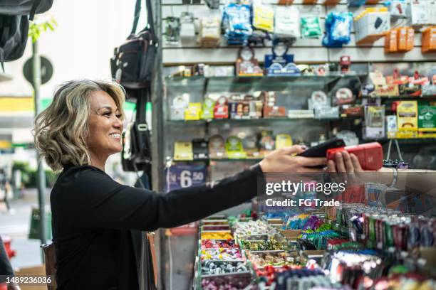mature woman paying with mobile phone in a newsstand - bubble gum stock pictures, royalty-free photos & images