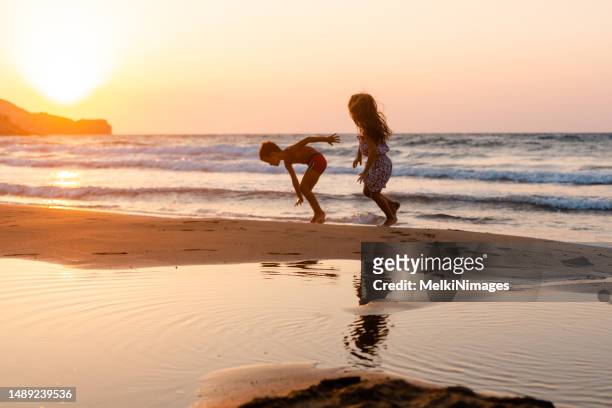 fröhliche kinder, die bei einem wunderschönen sonnenuntergang am strand spielen - children only stock-fotos und bilder