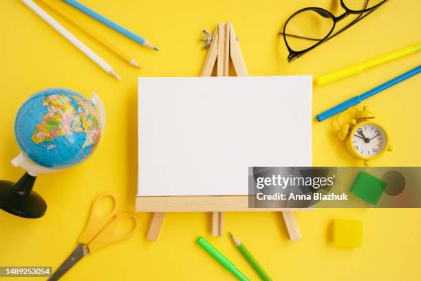 back to school concept. flat lay with easel, pencils, alarm clock, eraser, scissors, eyeglasses and globe over yellow background - écolier-garçon photos et images de collection