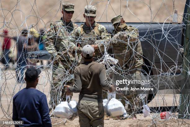 Texas National Guard soldiers close a section of razor wire surrounding a makeshift migrant camp as an immigrant tries to return with food for his...