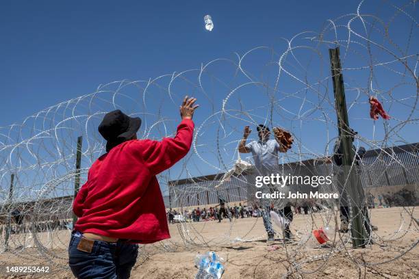 An immigrant throws bottles of water into a makeshift migrant camp at the U.S.-Mexico border fence on May 11, 2023 in El Paso, Texas. The number of...