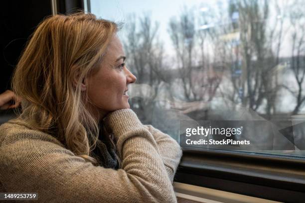 une femme monte dans un train et regarde par la fenêtre. - woman blond looking left window photos et images de collection