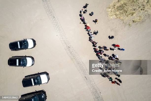In an aerial view, immigrants stand near razor wire and Texas state troopers while waiting to be processed for asylum claims within a makeshift...