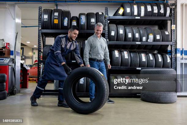 mécanicien changeant un pneu de voiture et parlant à son client au garage de réparation - partie de véhicule photos et images de collection