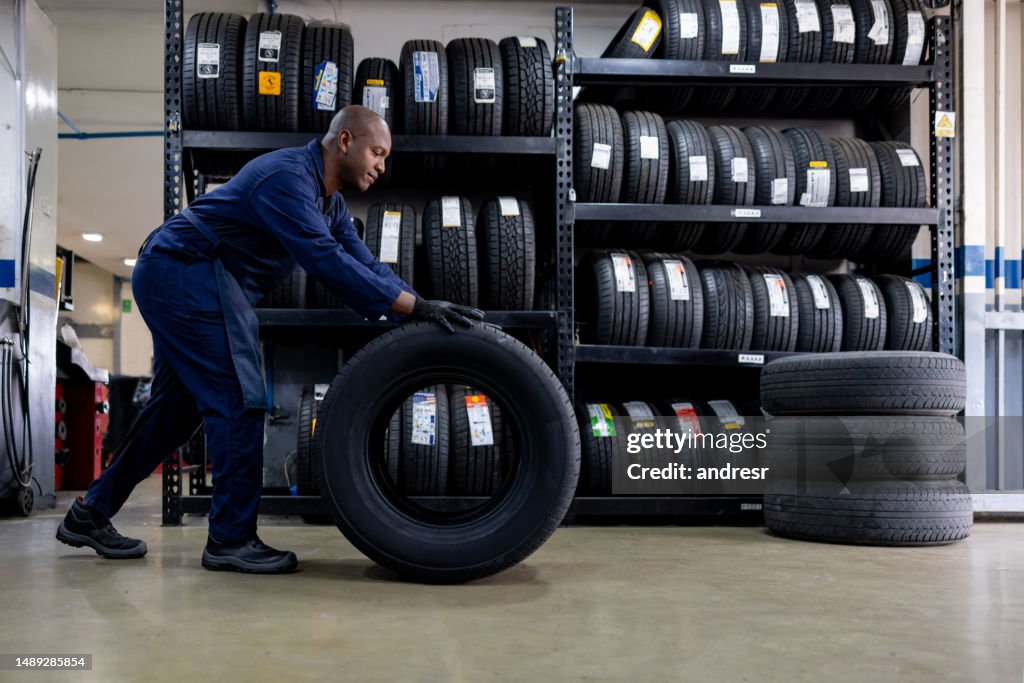 Mechanic changing a flat tire and carrying a wheel at a repair garage