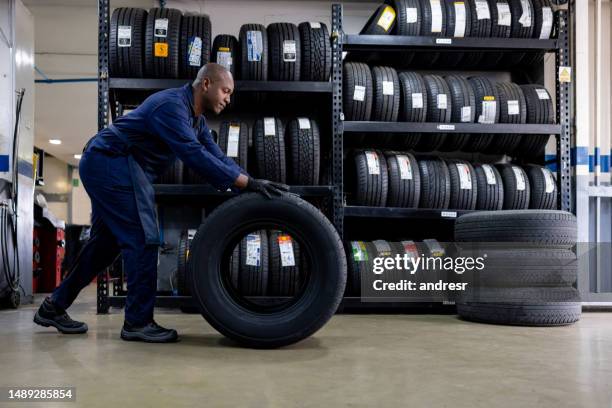 mechanic changing a flat tire and carrying a wheel at a repair garage - auto mechanic shop stock pictures, royalty-free photos & images