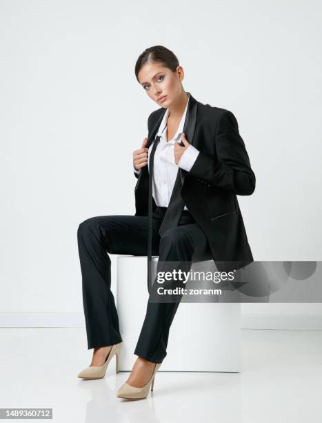 beautiful young woman in black pant suit and white button down shirt sitting and looking at camera - white suit and tie stock pictures, royalty-free photos & images