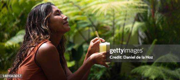 side view of asian filipino woman with eyes relaxing, enjoying healthy juice outdoors in nature. defocused background. copy space. wellness and relaxation - health retreat banner stock-fotos und bilder